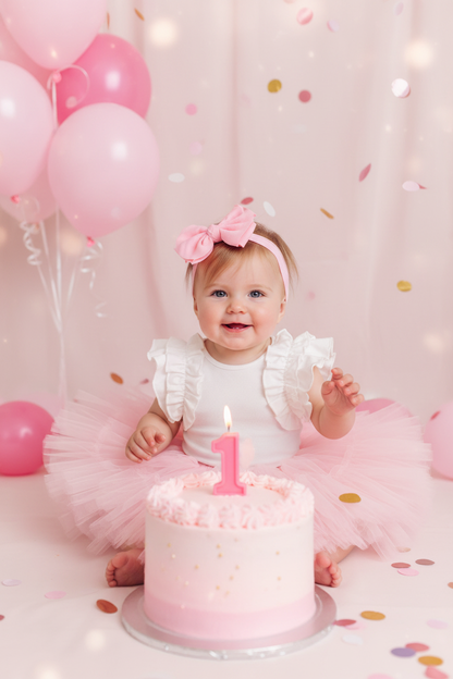 Baby girl wearing the White Ruffle Bodysuit with a pink tutu skirt at a pastel pink 1st birthday party